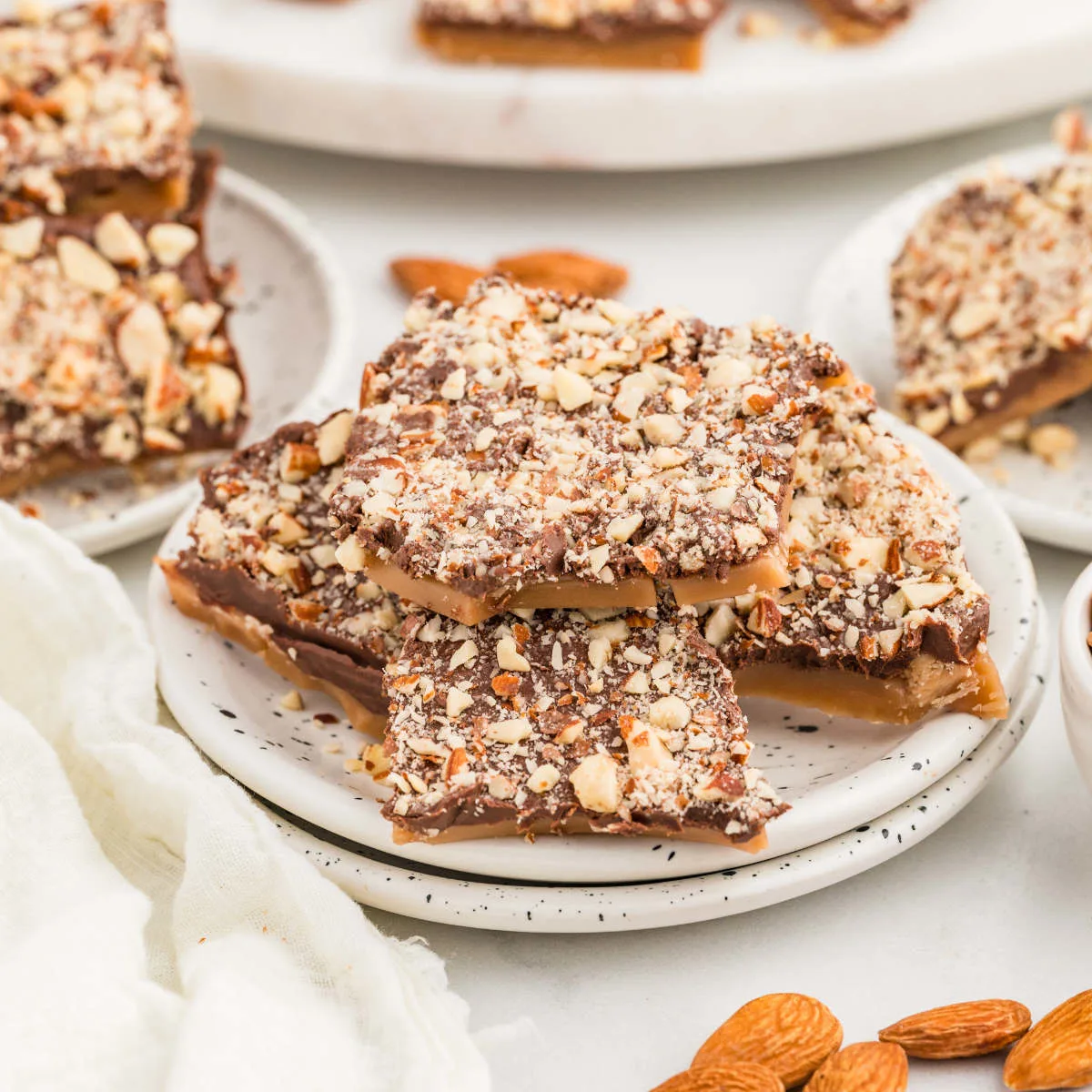 A plate with homemade English toffee candy next to some almonds.