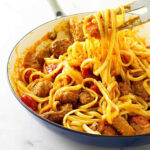 A fork picking up pasta with chorizo sausage from a skillet.