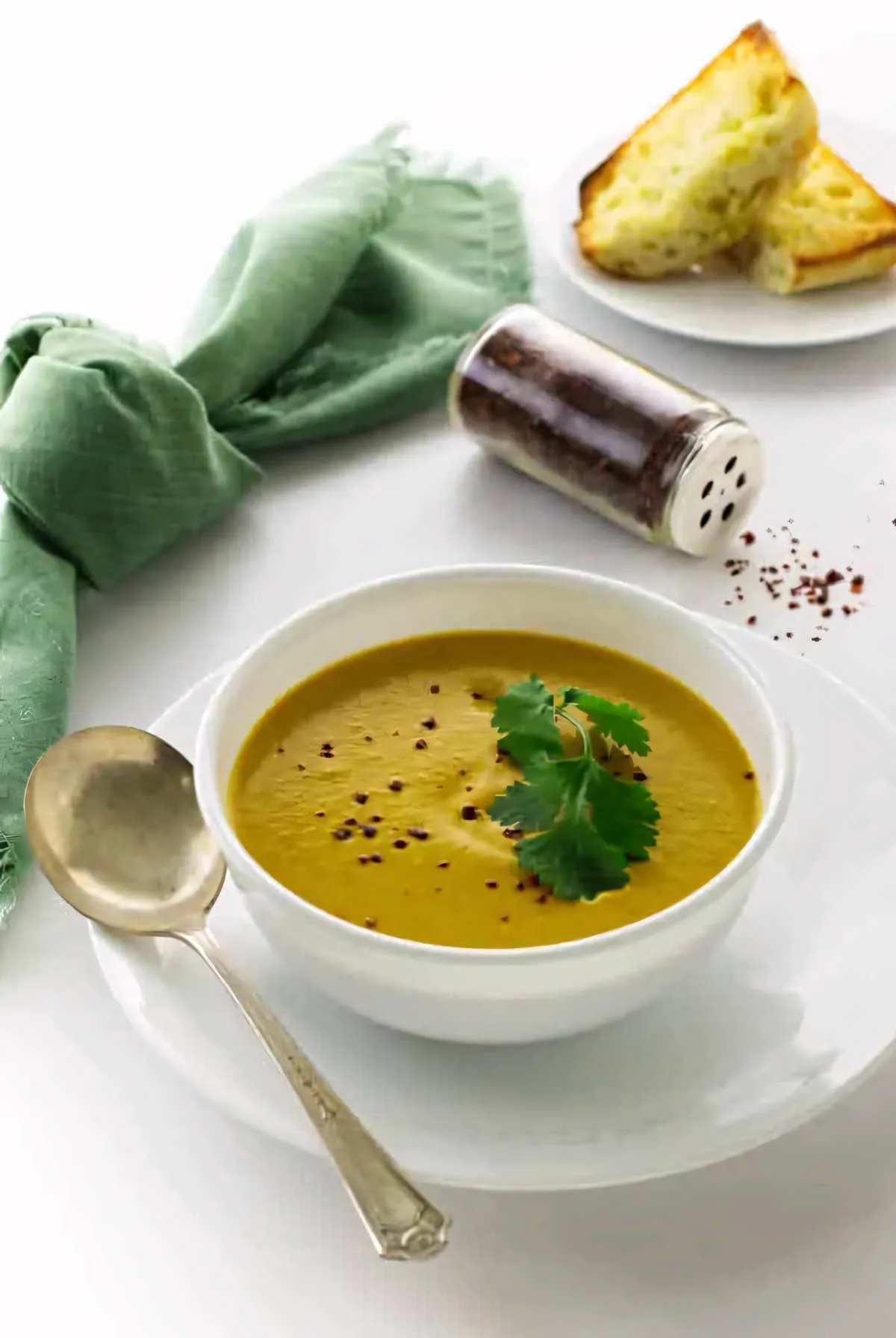 A bowl filled with creamy pumpkin soup with bread in the background.