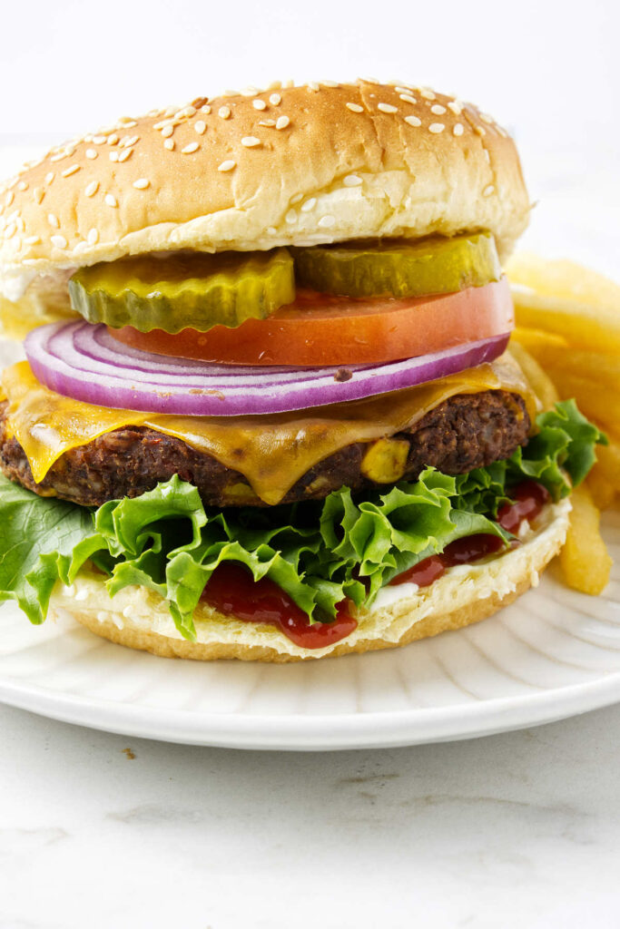 A black bean burger on a bun with lettuce, cheese, onion, tomato, and pickles.