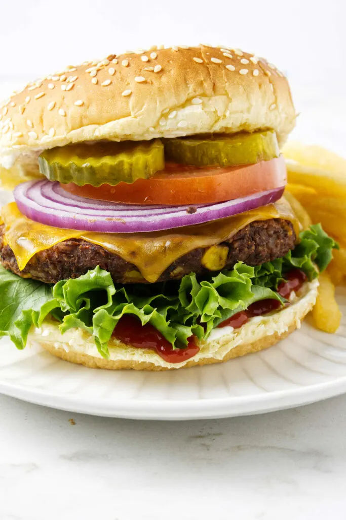 A black bean burger on a bun with lettuce, cheese, onion, tomato, and pickles.