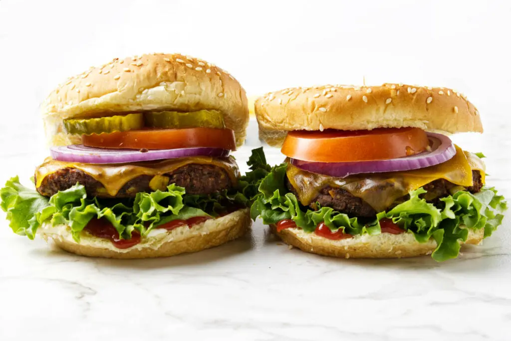 Two burgers next to each other with lettuce, onion, and tomatoes.