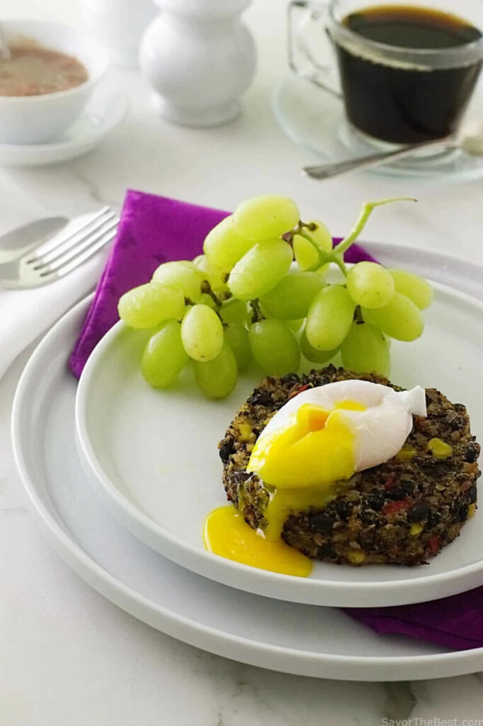 A bean and quinoa burger topped with a soft poached egg next to green grapes.