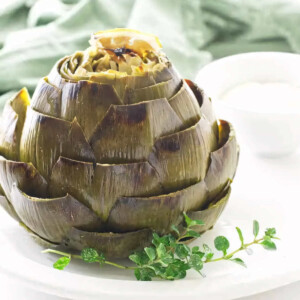 A garlic roasted artichoke on a plate with a sprig of thyme.