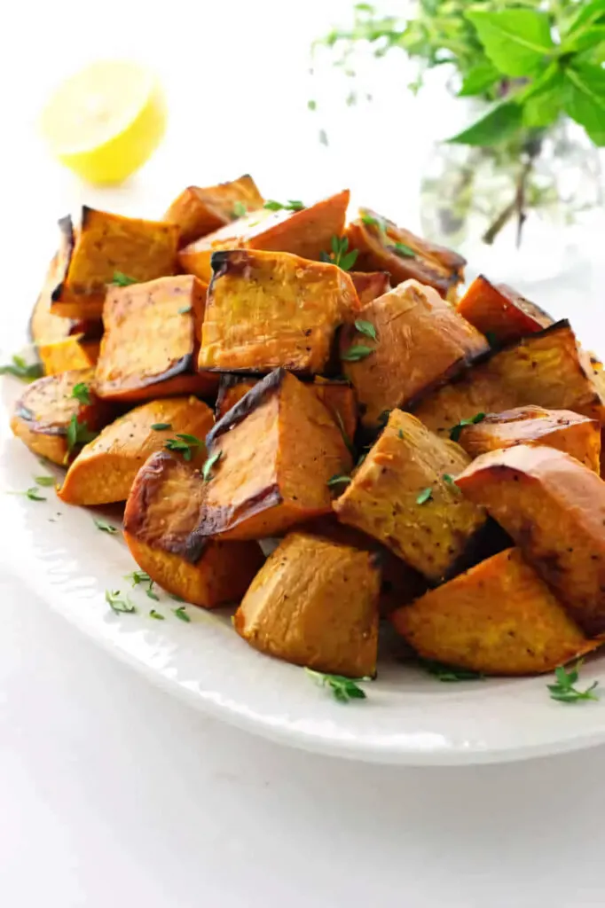 A side dish of roasted sweet potatoes next to herbs and lemon.