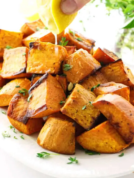 Squeezing a lemon over a cubes of roasted sweet potatoes.