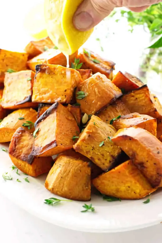 Squeezing a lemon over a cubes of roasted sweet potatoes.