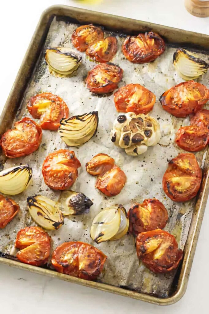 Roasted tomatoes and onions on a baking sheet.