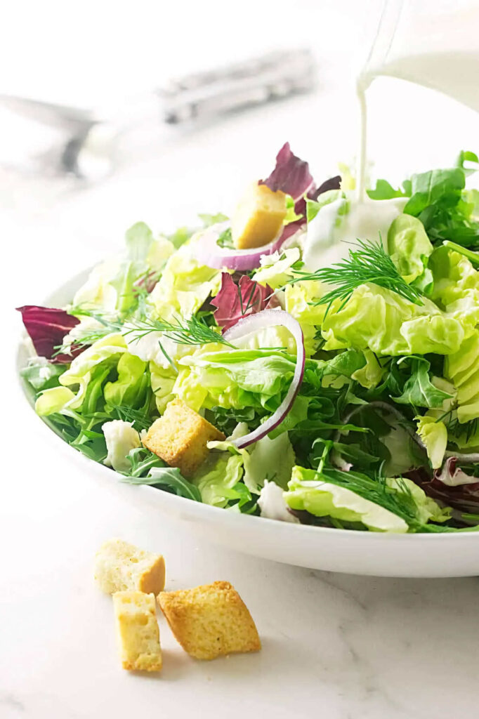 Pouring blue cheese dressing on salad greens.