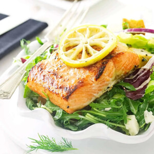 A salad plate filled with salmon and salad greens with bread in the background.