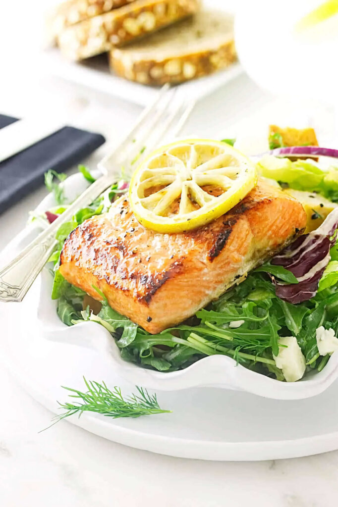 A salad plate filled with salmon and salad greens with bread in the background.