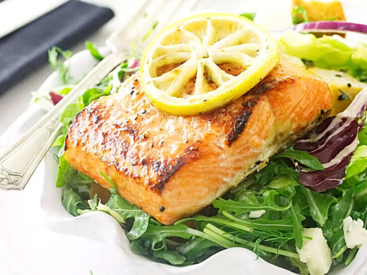 A salad plate filled with salmon and salad greens with bread in the background.