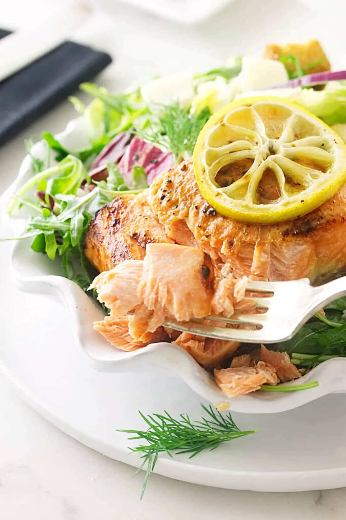 A fork flaking off a salmon on a salad plate.