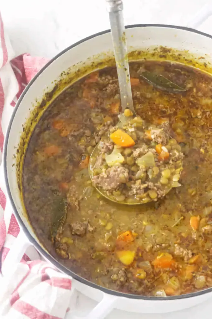 A ladle scooping soup from a Dutch oven pot.