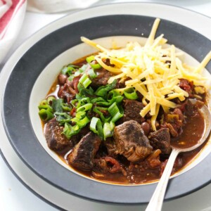 A bowl of chunky beef chili topped with chives and beans.