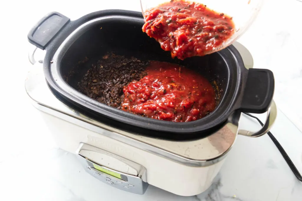 Pouring tomato sauce into the crockpot.