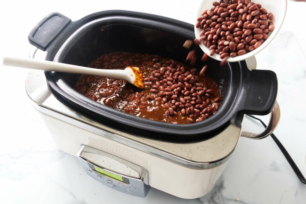 Pouring red beans into a crockpot filled with chili.