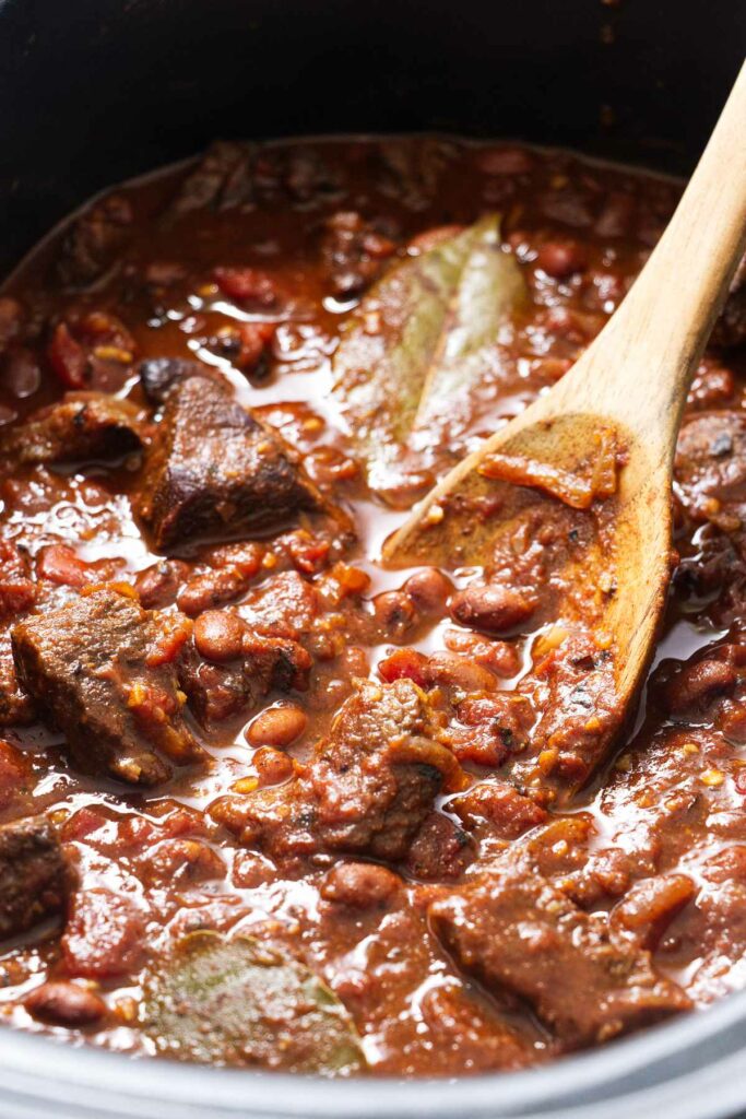 A wooden spoon scooping a serving of chili with beef and beans.