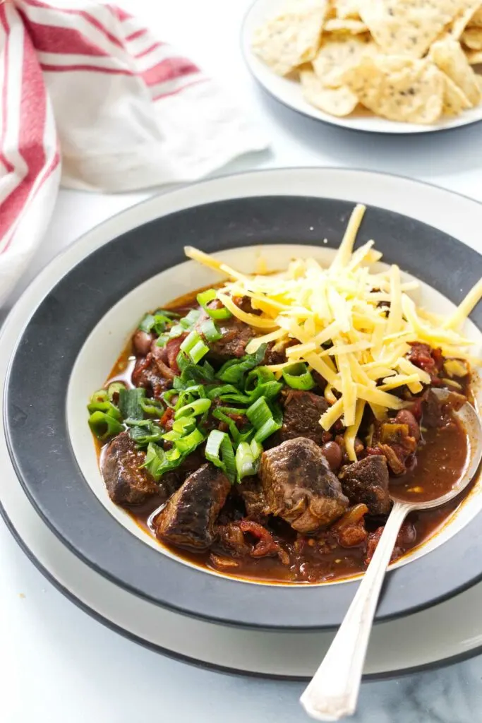 A serving bowl filled with beef chili beans and a bowl of tortilla chips in the background.