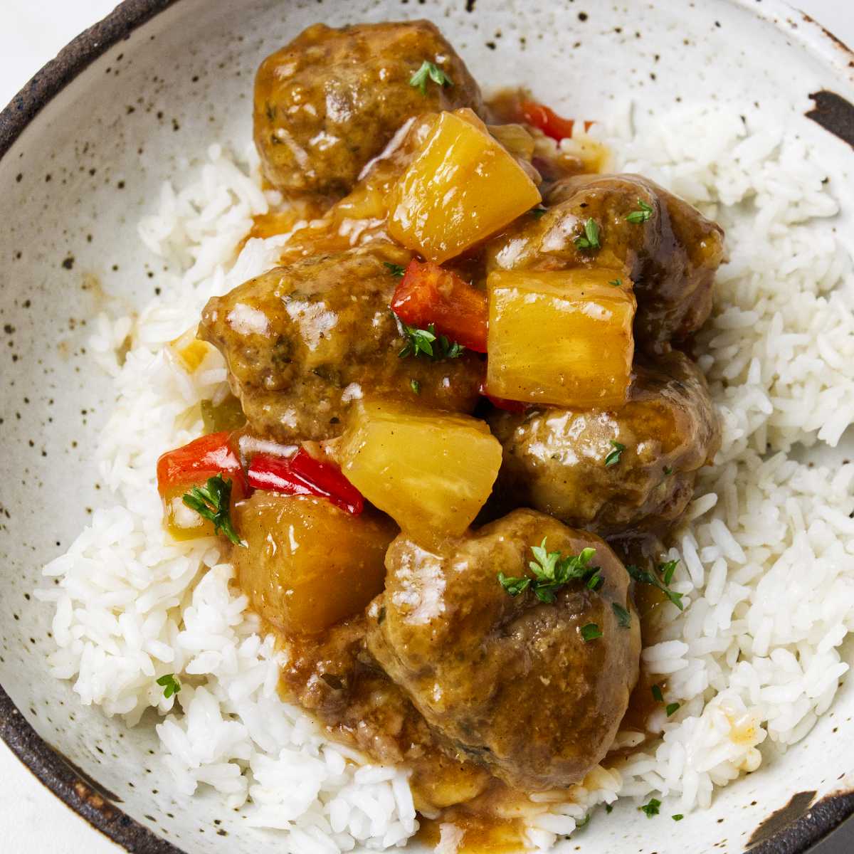 A bowl of sweet and sour meatballs on a bed of white rice.