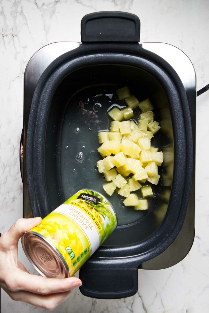 Adding pineapple chunks to a slow cooker.