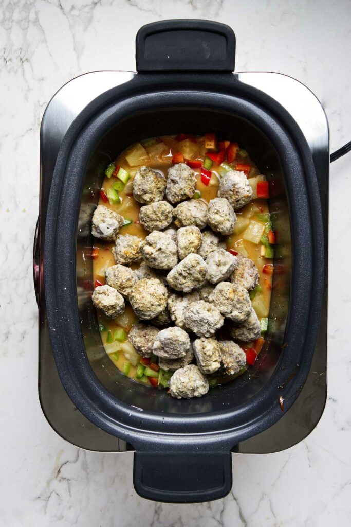 Placing the frozen meatballs on the sweet and sour mixture in the crock pot.