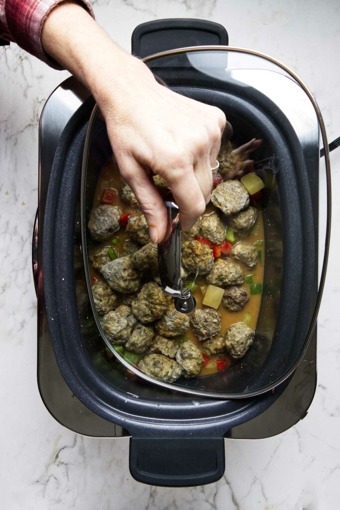 Placing the lid on the crockpot to cook the meatballs.