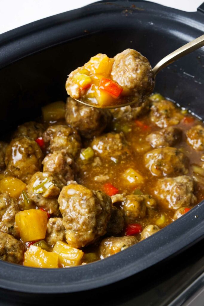 Scooping scooping a serving of Slow cooker sweet and sour meatballs from the crockpot.