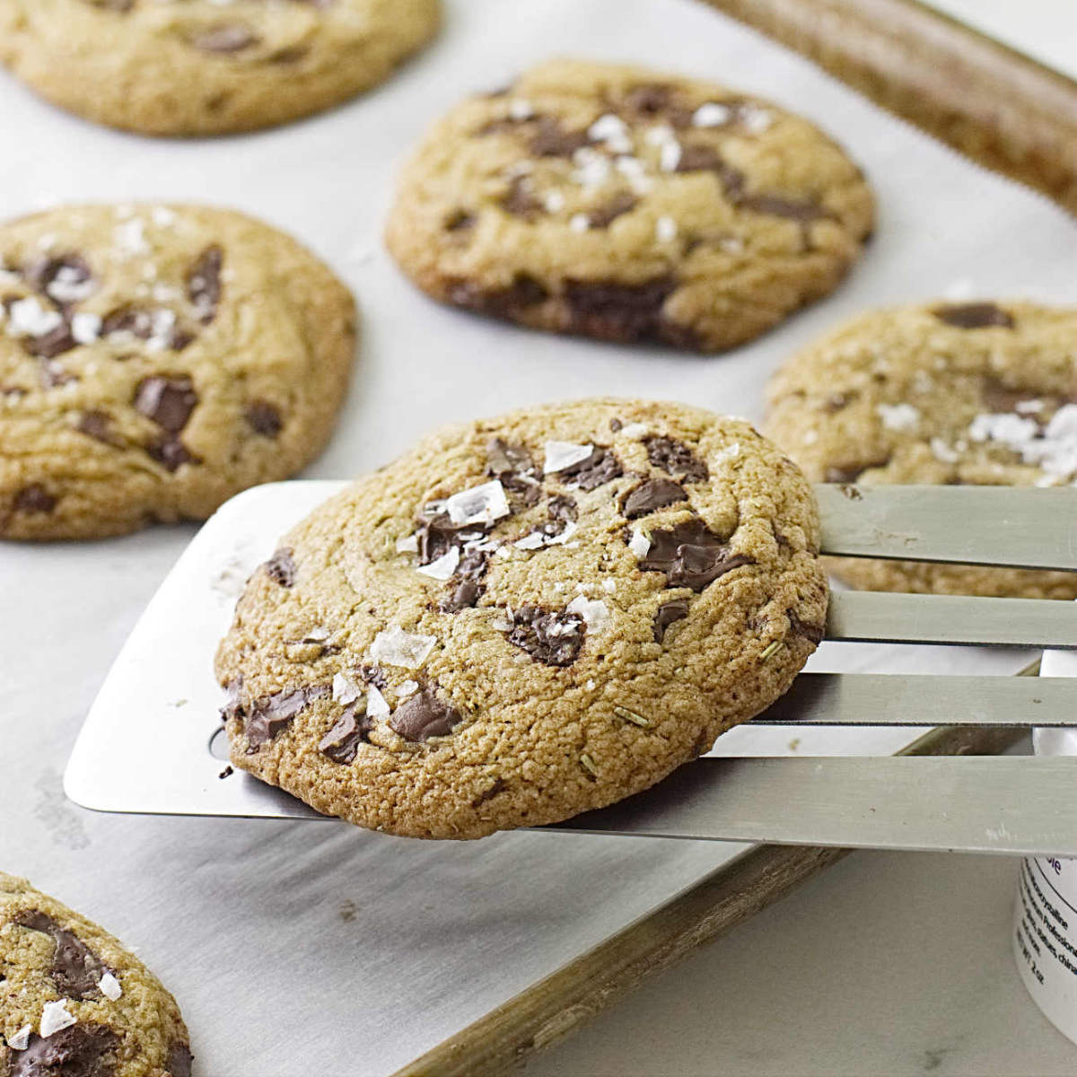 A spatula lifting a chocolate chunk cookie off a baking sheet.