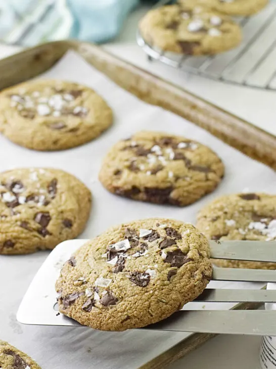 A metal spatula lifting cookies off a baking pan.