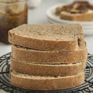 Four slices of bread made with sprouted wheat flour stacked on each other with jam in the background.