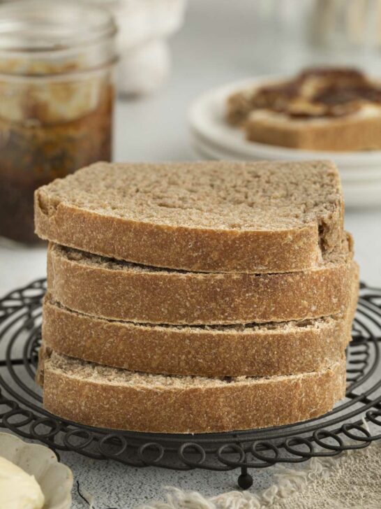 Four slices of bread made with sprouted wheat flour stacked on each other with jam in the background.