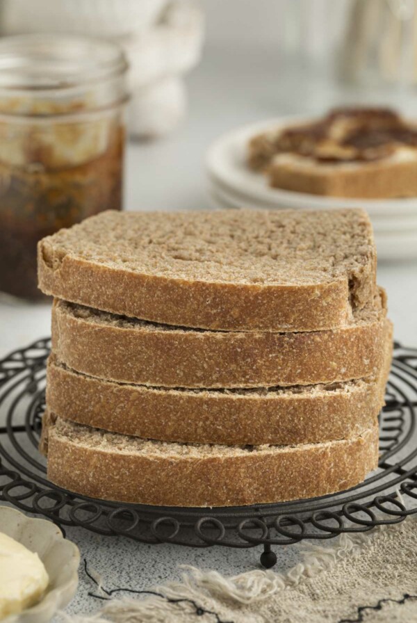 Four slices of bread made with sprouted wheat flour stacked on each other with jam in the background.