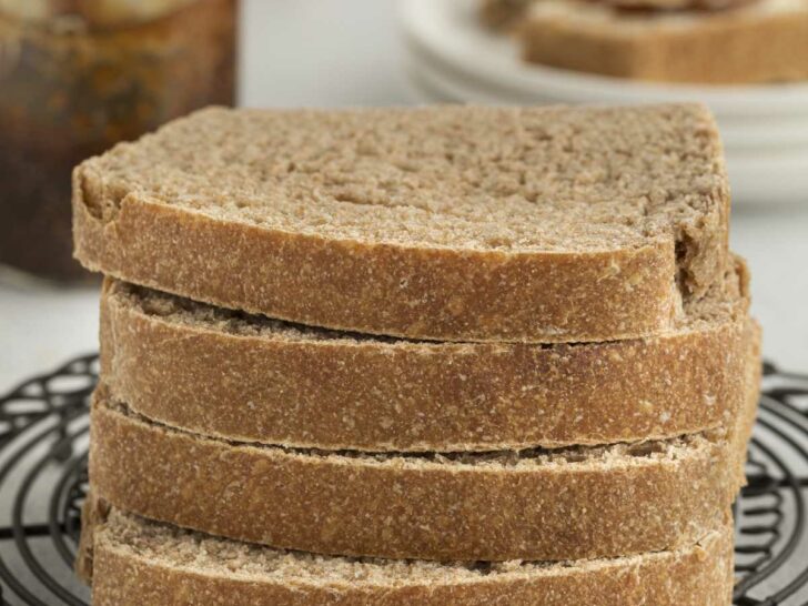 Four slices of bread made with sprouted wheat flour stacked on each other with jam in the background.