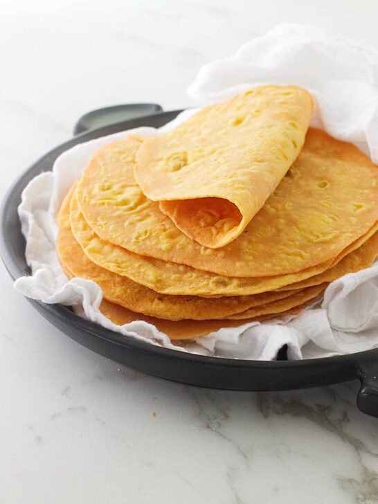 A stack of sweet potato flatbread on a black serving dish with a white tea towel.