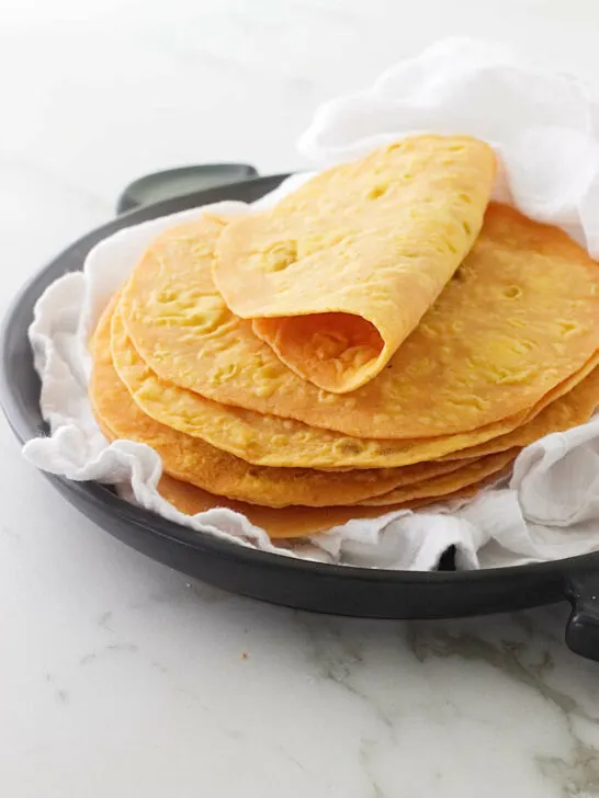 A stack of sweet potato flatbread on a black serving dish with a white tea towel.