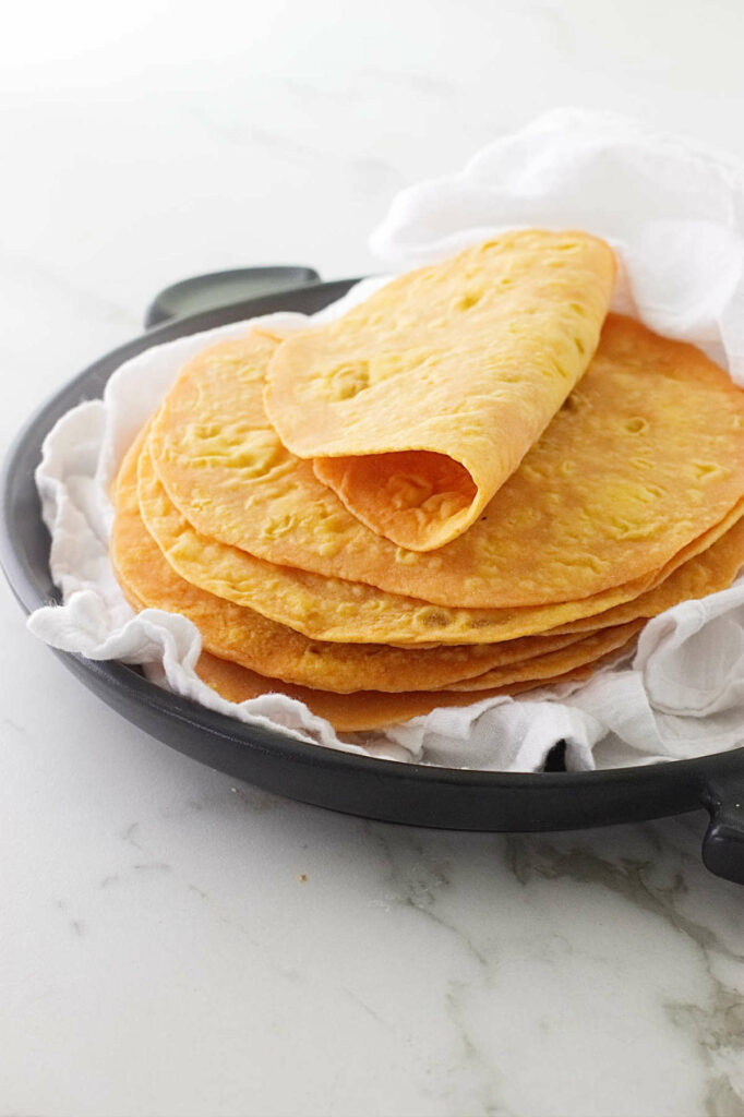 A stack of sweet potato flatbread on a black serving dish with a white tea towel.