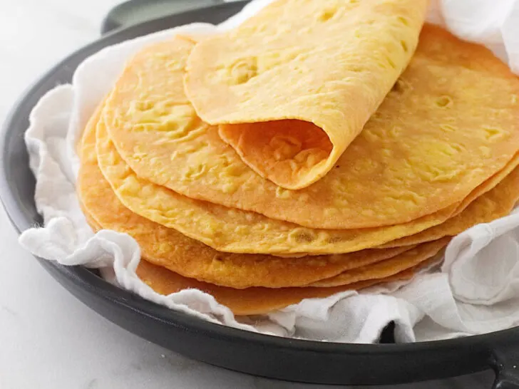 A stack of sweet potato flatbread on a black serving dish with a white tea towel.