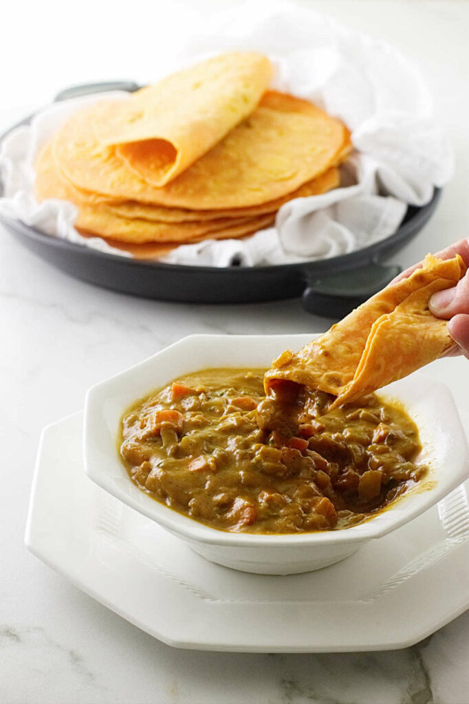 A rolled up sweet potato roti being dipped in lentil soup.