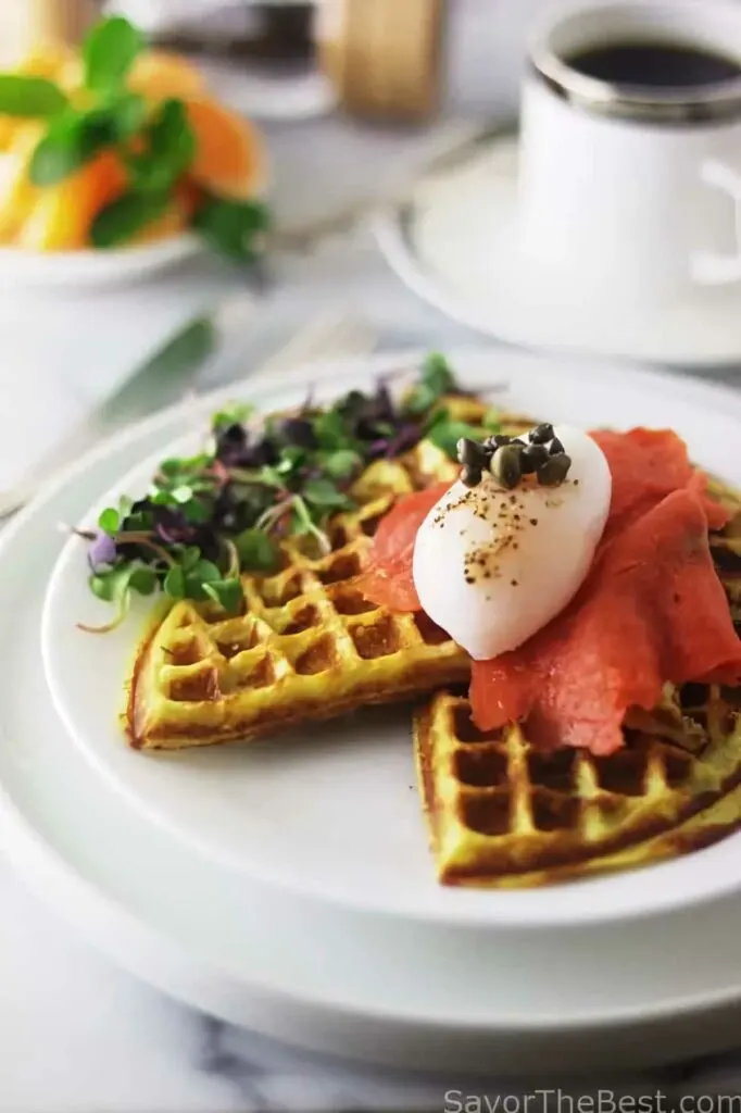 A plate filled with sweet potato waffles and smoked salmon with a cup of coffee in the background.