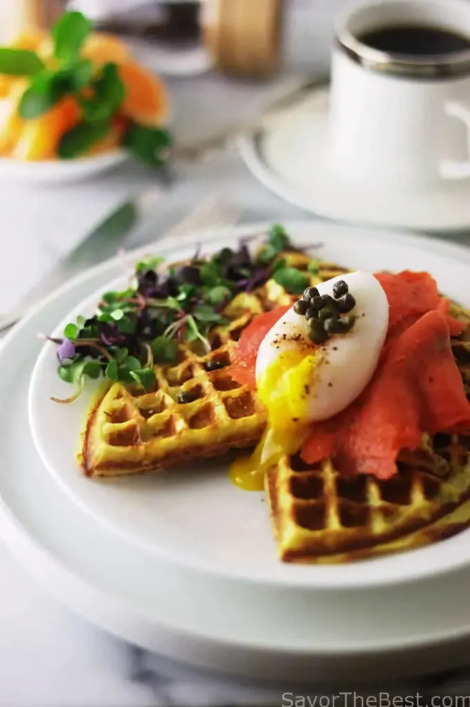 A sweet potato waffle topped with smoked salmon and an egg in front of a cup of coffee.