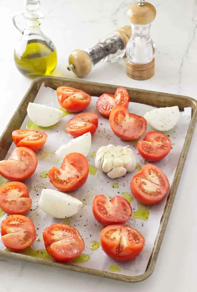 Spreading sliced tomatoes, onions, and garlic out on a baking sheet to roast for soup.