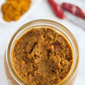 A mason jar filled with yellow curry paste next to dried red chilies.