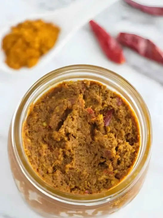 A mason jar filled with yellow curry paste next to dried red chilies.