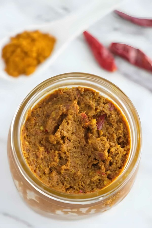 A mason jar filled with yellow curry paste next to dried red chilies.