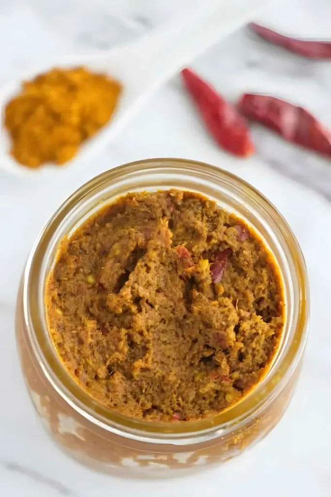 A mason jar filled with yellow curry paste next to dried red chilies.