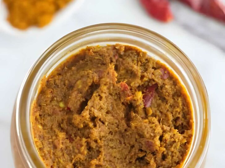 A mason jar filled with yellow curry paste next to dried red chilies.