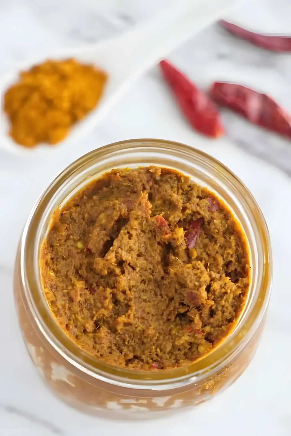 A mason jar filled with yellow curry paste next to dried red chilies.