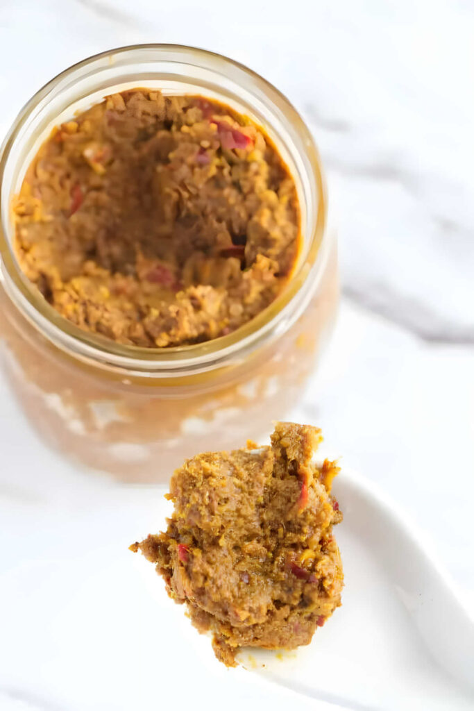 A spoon scooping out curry paste from a jar.