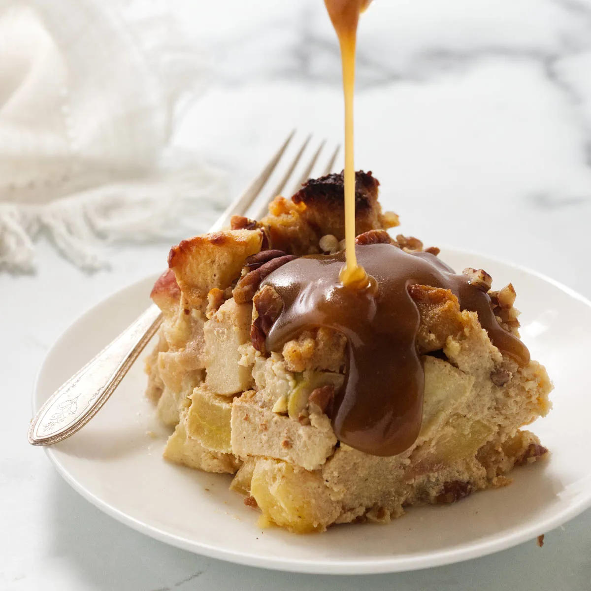 Pouring maple cream sauce over a slice of apple pecan bread pudding.